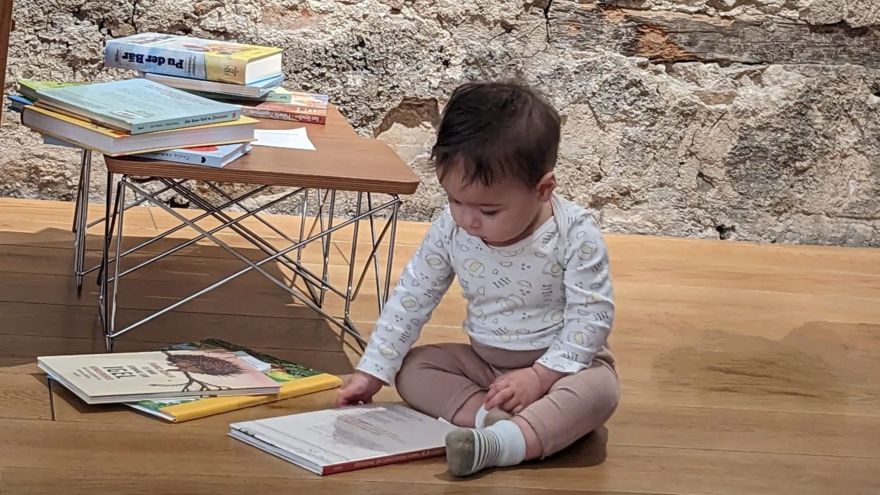 Ein kleines Kind sitzt auf dem Fußboden und blättert in einem Buch.
