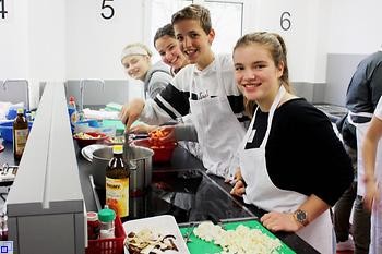 Drei Mädchen und ein Junge sind gemeinsam in der Küche am Arbeiten und Mithelfen
