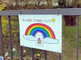 Bild mit buntem Regenbogen und der Aufschrift "Alles wird gut" hängt an einem Zugangstor