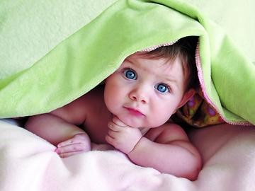 Baby mit Teppich über dem Kopf schaut in die Kamera