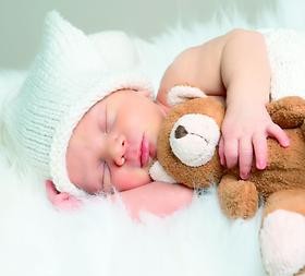Ein Baby schläft mit einem Kuscheltier im Arm