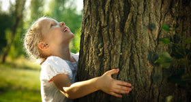 Ein Mädchen umarmt fröhlich einen Baumstamm