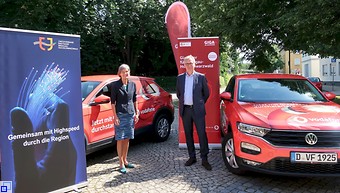 Die Landrätin und Herr Scharfe stehen mit Werbebannern und zwei Vodafone-Autos vor dem Landratsamt.