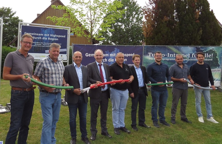 Die neun Beteiligten stehen nebeneinander und halten ein Breitbandkabel.