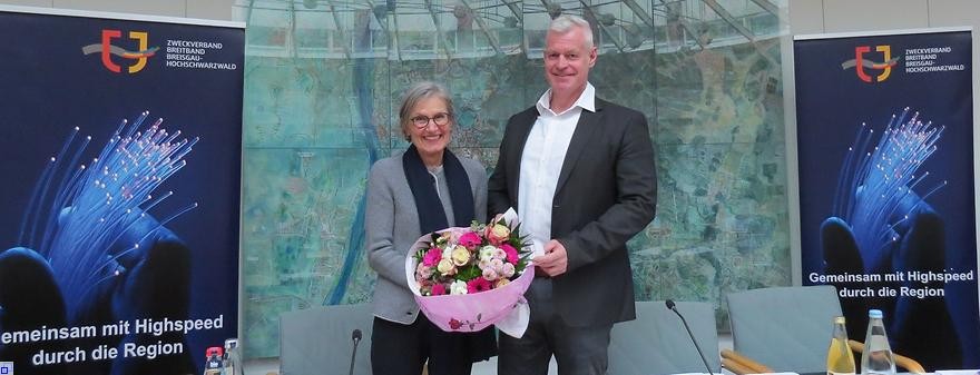 Die Landrätin mit einem großen Blumenstrauß und Herr Rein stehen auf dem Podium des Sitzungssaales und Lächeln